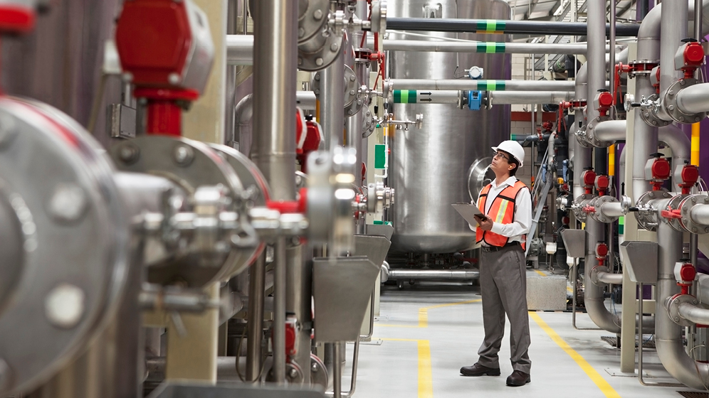 An engineer studies large silver tanks on a warehouse floor. 