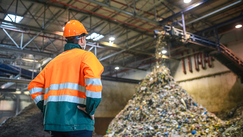 A man is looking at garbage being dumped at a factory.