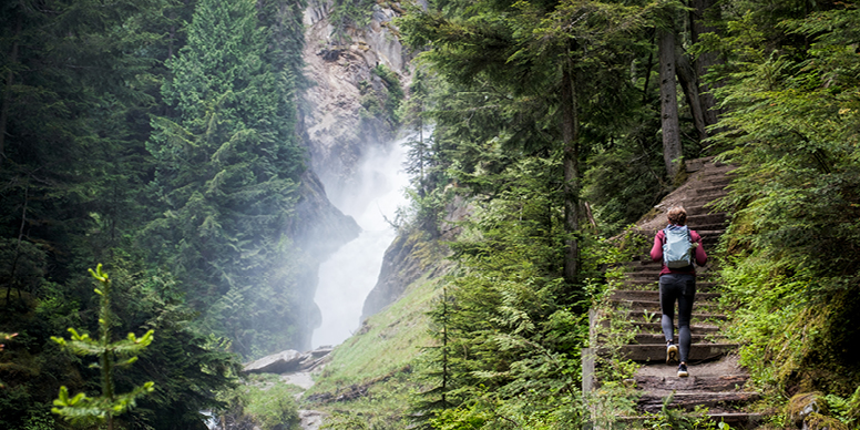 Female hiker walking up stairs within a forest while admiring a waterfall. 