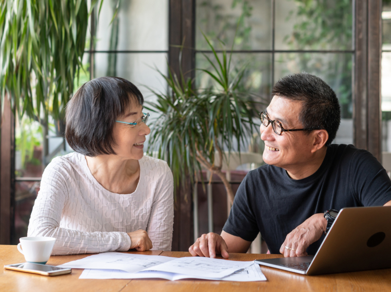 Older couple smiling at one another next to papers and a laptop.