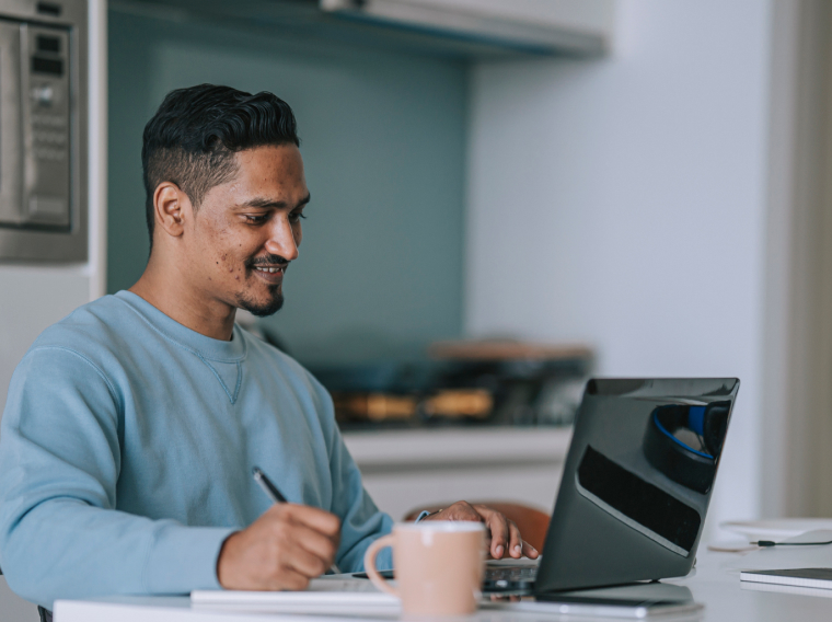 Man sitting down and writing next to his laptop